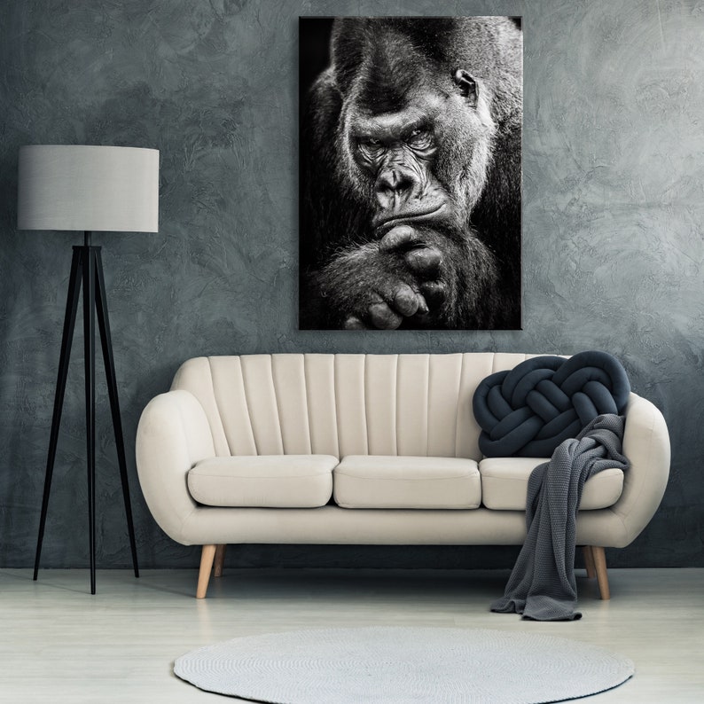 May include: Black and white photograph of a gorilla looking directly at the camera. The gorilla is sitting with its chin resting on its hand. The photo is printed on canvas and framed.