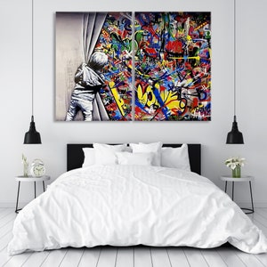 Op de afbeelding: Een gesplitst canvas schilderij dat een kind laat zien dat door een wit gordijn naar een kleurrijke graffitimuur kijkt. De graffiti heeft een verscheidenheid aan kleuren, waaronder rood, geel, blauw, groen en zwart. Het kind draagt een wit shirt en een blauwe jeans.