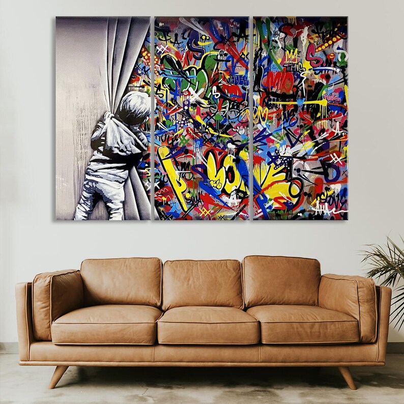 Op de afbeelding: Een driedelig canvasprint met een kind dat door een wit gordijn gluurt. De achtergrond is een kleurrijke graffitimuur met levendige kleuren en abstracte vormen.