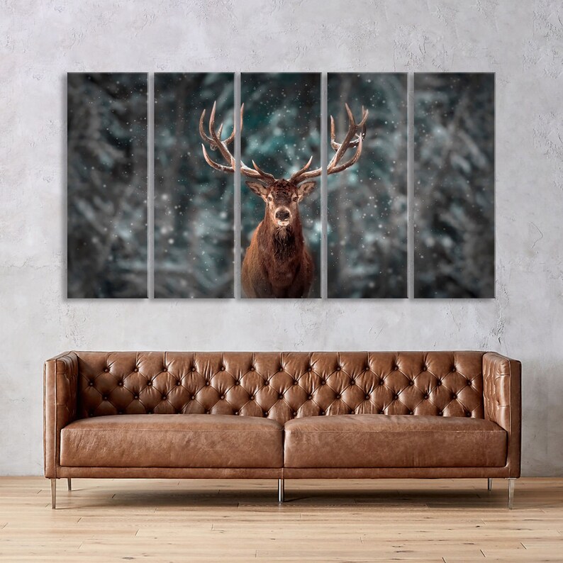 May include: A brown deer with large antlers stands in a snowy forest. The deer is looking directly at the camera. The background is blurred and out of focus.