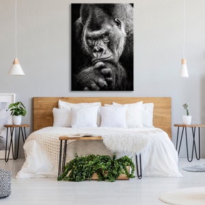 May include: Black and white photograph of a gorilla looking directly at the camera. The gorilla is sitting with its arms crossed and has a serious expression on its face.