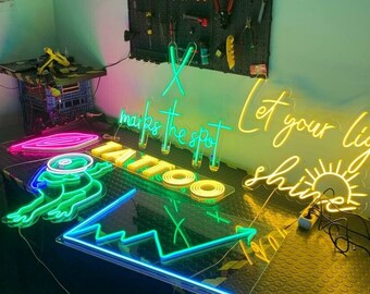 May include: A collection of neon signs with various designs, including a frog, an arrow, a sun, and the words "X marks the spot" and "Let your light shine".