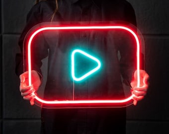 May include: A person holding a neon sign shaped like a play button. The sign is red with a blue play button inside.