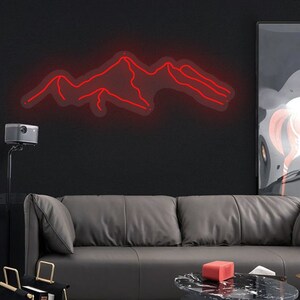 May include: A red neon sign depicting a mountain range, hanging on a black wall above a grey leather sofa. The sign is lit and glowing, casting a warm red light on the wall.