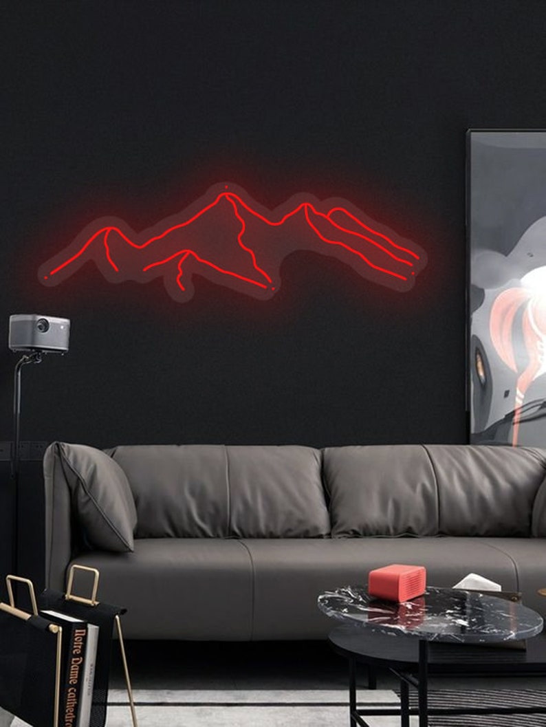 May include: A red neon sign depicting a mountain range, hanging on a black wall above a grey leather sofa. The sign is lit and glowing, casting a warm red light on the wall.