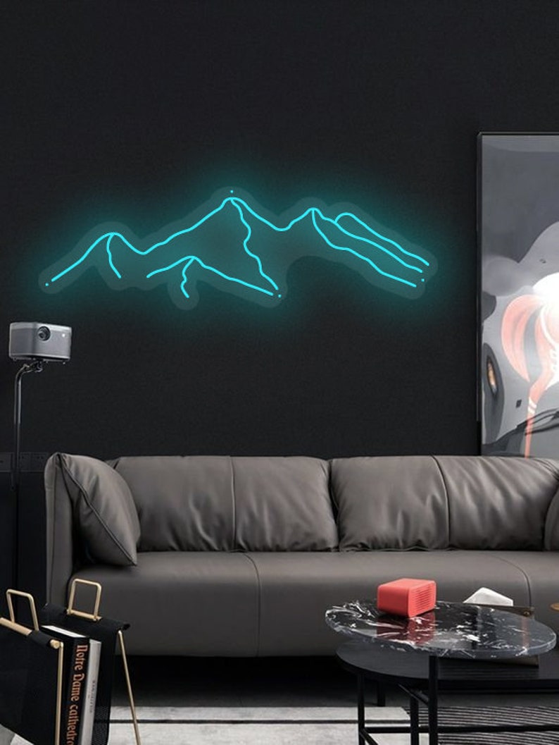May include: A teal blue neon sign depicting a mountain range on a black wall. The sign is hanging above a grey leather sofa and a black coffee table.