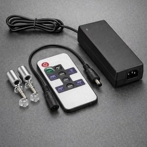 May include: A black power adapter, remote control, and mounting hardware are displayed on a gray surface. The white remote has several buttons and a power button. Two silver mounting bolts are also visible.