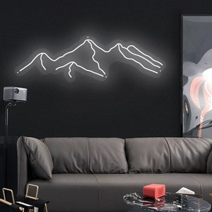 May include: A white neon sign depicting a mountain range, hanging on a black wall above a grey leather sofa. The sofa is in a living room setting with a coffee table and a black and white framed picture on the wall.