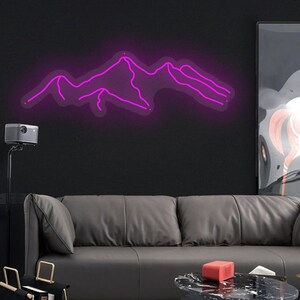 May include: A pink neon sign depicting a mountain range. The sign is mounted on a black wall above a grey leather sofa.