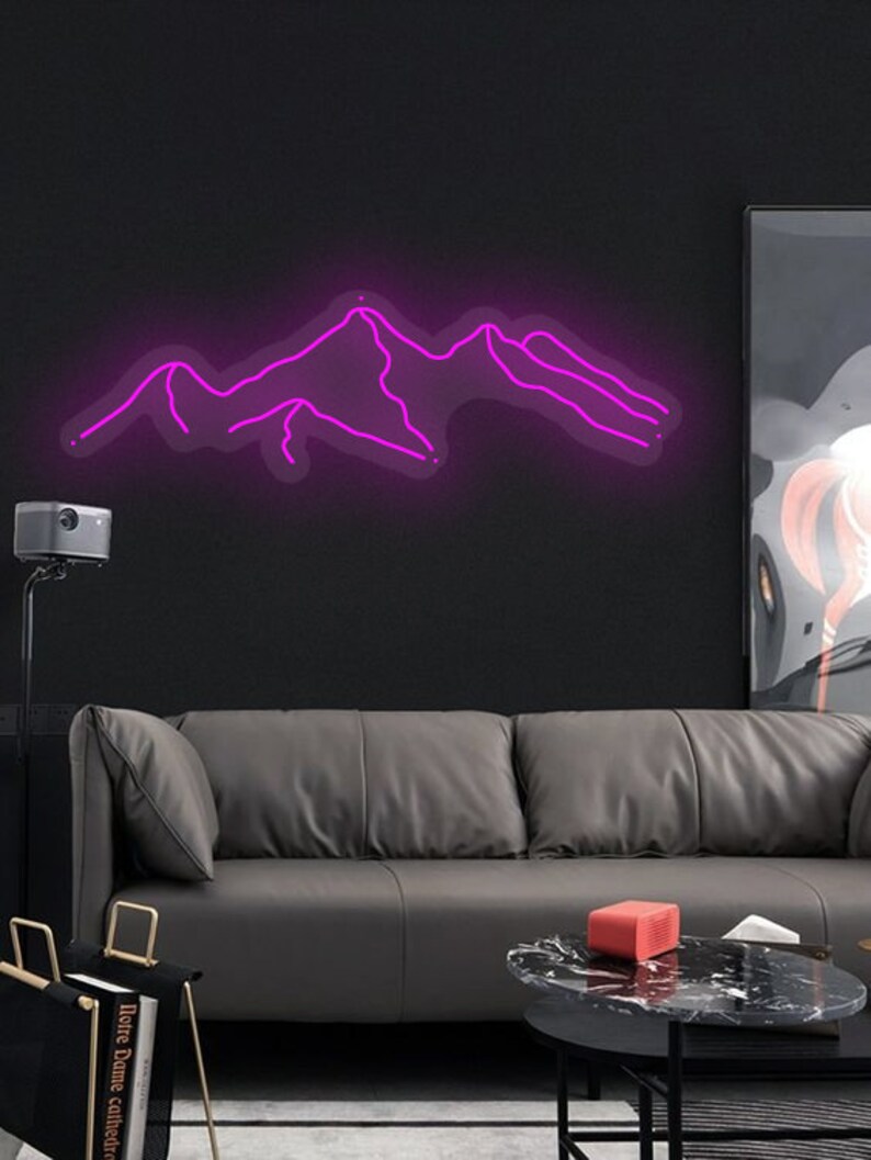 May include: A pink neon sign depicting a mountain range. The sign is mounted on a black wall above a grey leather sofa.
