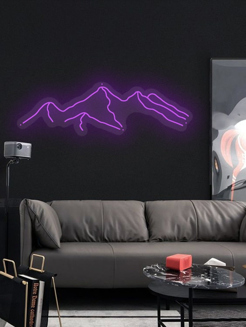 May include: A purple neon sign depicting a mountain range silhouette. The sign is mounted on a black wall above a grey leather sofa.