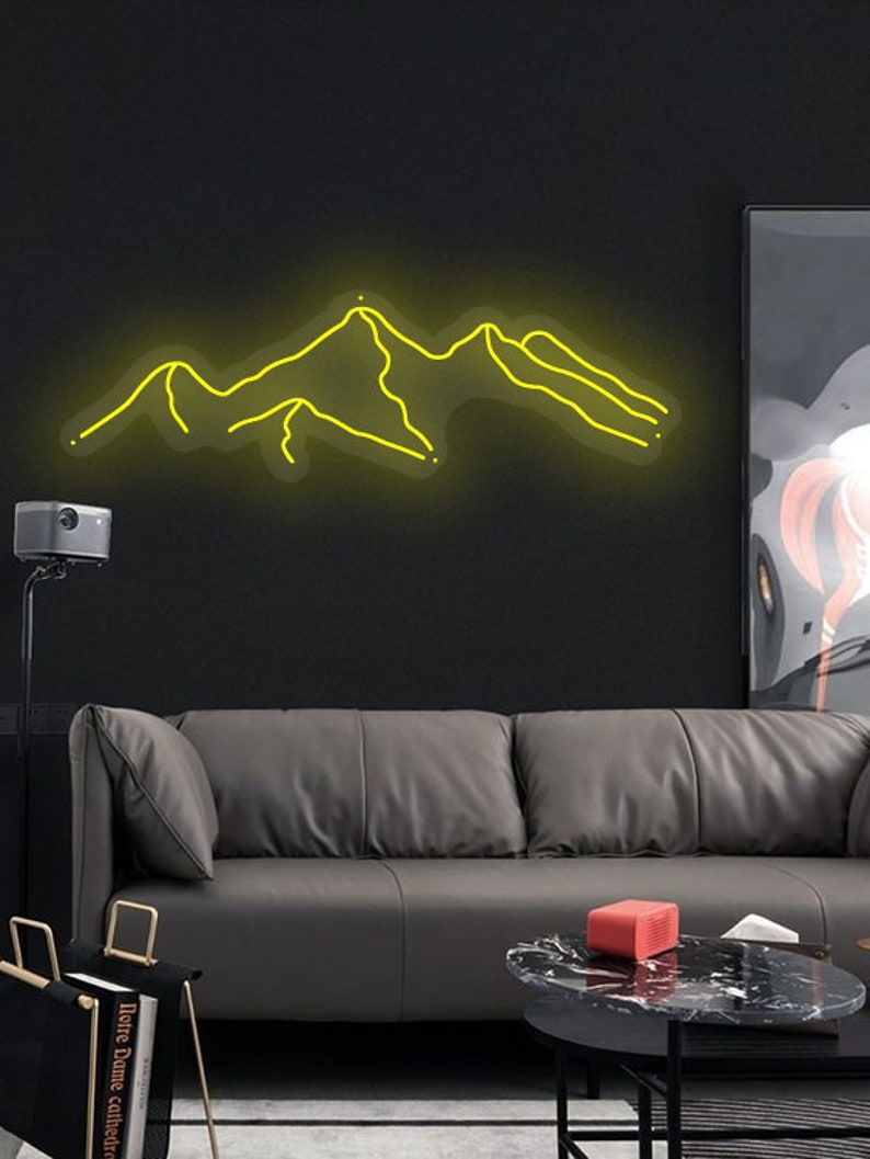 May include: A yellow neon sign depicting a mountain range on a black wall. The sign is mounted above a grey leather sofa and a black coffee table.