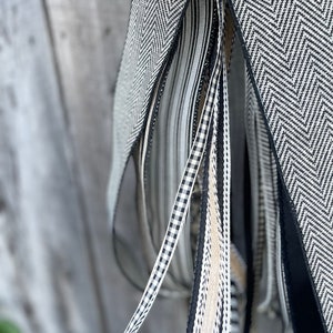 K&ouml;nnte beinhalten: Nahaufnahme einer Sammlung dekorativer B&auml;nder in verschiedenen Mustern und Texturen. Die B&auml;nder weisen schwarz-wei&szlig;e Designs auf, darunter Fischgr&auml;tenmuster, Streifen und Vichy-Karo. Einige B&auml;nder sind einfarbig schwarz oder beige. Die B&auml;nder werden wahrscheinlich zum Basteln oder Dekorieren verwendet.