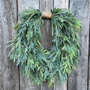 May include: A green leafy wreath with a burlap bow hanging on a wooden door.