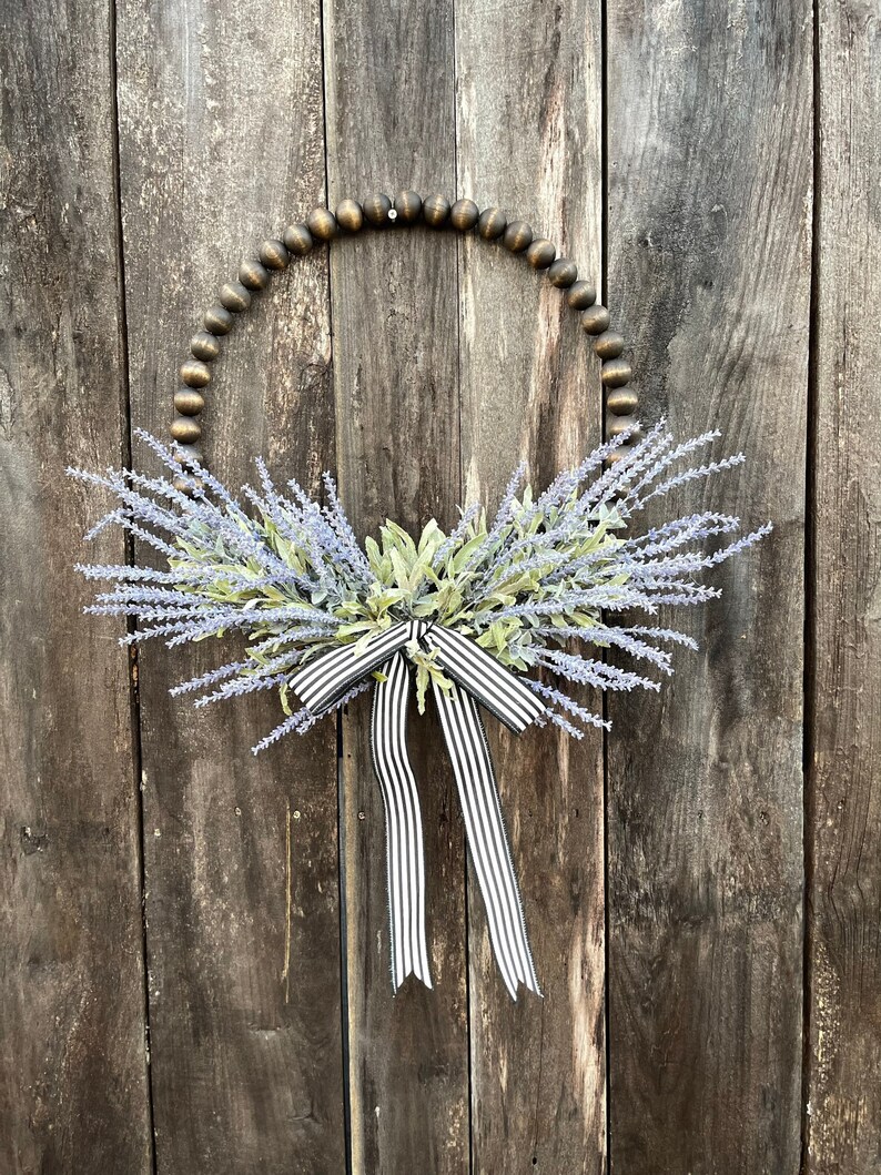 May include: A lavender wreath with a black and white striped ribbon on a wooden background.