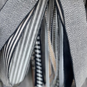 K&ouml;nnte beinhalten: Nahaufnahme von dekorativen B&auml;ndern in verschiedenen Mustern. Die B&auml;nder weisen schwarz-wei&szlig;e Designs auf, darunter Fischgr&auml;tenmuster, Streifen und Karos. Einige B&auml;nder sind einfarbig schwarz oder beige. Die B&auml;nder werden wahrscheinlich zum Basteln oder zum Verpacken von Geschenken verwendet.