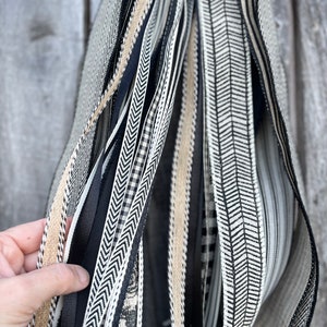 K&ouml;nnte beinhalten: Eine Sammlung dekorativer B&auml;nder in verschiedenen Mustern und Texturen. Die B&auml;nder umfassen Schwarz-, Wei&szlig;- und Beiget&ouml;ne mit Designs wie Fischgr&auml;tenmuster, Streifen und floralen Mustern. Die B&auml;nder werden zusammengehalten, wodurch ein geschichteter Effekt entsteht.