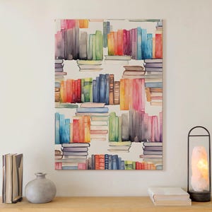 May include: Watercolor painting of a bookshelf with stacks of books in various colors. The artwork features a vibrant palette of blues, reds, greens, and yellows. The painting is displayed on a white wall above a wooden surface.