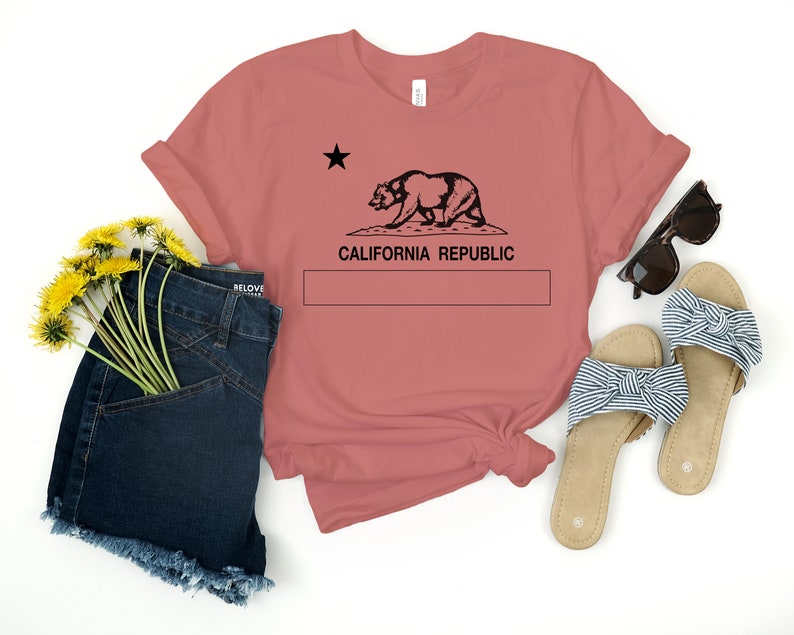 May include: A dusty rose t-shirt with a black graphic of the California Republic flag featuring a bear and a star. The text "CALIFORNIA REPUBLIC" is printed below the graphic.