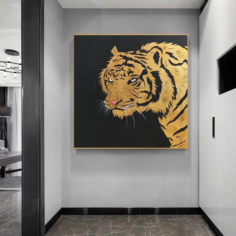 A gold tiger head on a black background. The tiger's eyes are black and the nose is pink. The tiger's fur is detailed with gold paint.