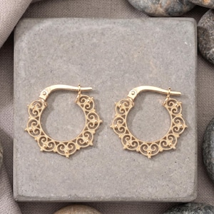 May include: A pair of gold hoop earrings featuring an intricate filigree pattern along the outer edge. The circular design includes delicate scrollwork and small bead accents, with a hinged post closure mechanism visible at the top of each hoop.