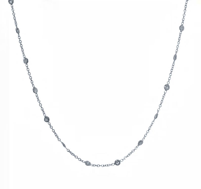 May include: A delicate silver necklace featuring a series of small, round, clear gemstones evenly spaced along a fine chain. The gemstones appear to be set in a bezel setting, and the necklace is displayed against a white background.