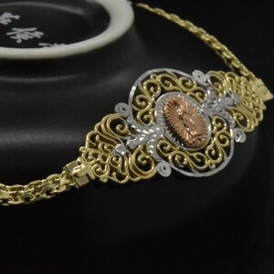 May include: A gold chain necklace with a filigree pendant featuring a religious image in the center. The pendant is made of gold, silver, and rose gold.