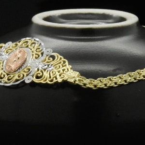 May include: A gold chain necklace with a filigree pendant featuring a rose gold center. The pendant is ornate and detailed, with a delicate design.