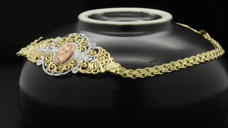 May include: A gold chain necklace with a filigree pendant featuring a rose gold center. The pendant is ornate and detailed, with a delicate design.