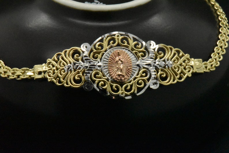 May include: A gold and silver filigree necklace with a round pendant featuring a religious figure. The pendant is made of rose gold and has a detailed design.