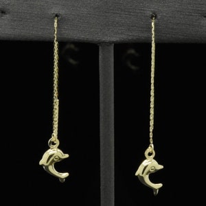 Può includere: Un paio di orecchini pendenti in oro a forma di delfino con una catena delicata. I delfini sono rivolti in avanti con le code arrotolate.