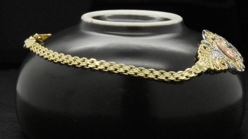 May include: A gold chain bracelet with a three-toned pendant. The pendant is a floral design with a center stone.