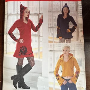 Peut inclure: Patron de couture Simplicity 1251 pour hauts et robes à capuche. L'enveloppe présente trois variantes : une robe rouge à capuche avec des motifs de roses noires, un haut bleu foncé à capuche et un haut jaune à capuche avec des manches fleuries.