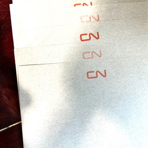 Puede incluir: Pila de seis hojas de papel blanco con la palabra "CN" impresa en rojo en cada hoja.