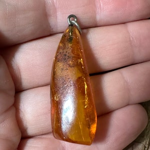 May include: A teardrop-shaped amber pendant with a silver bail. The amber is a warm, honey colour with inclusions of air bubbles and other organic matter.
