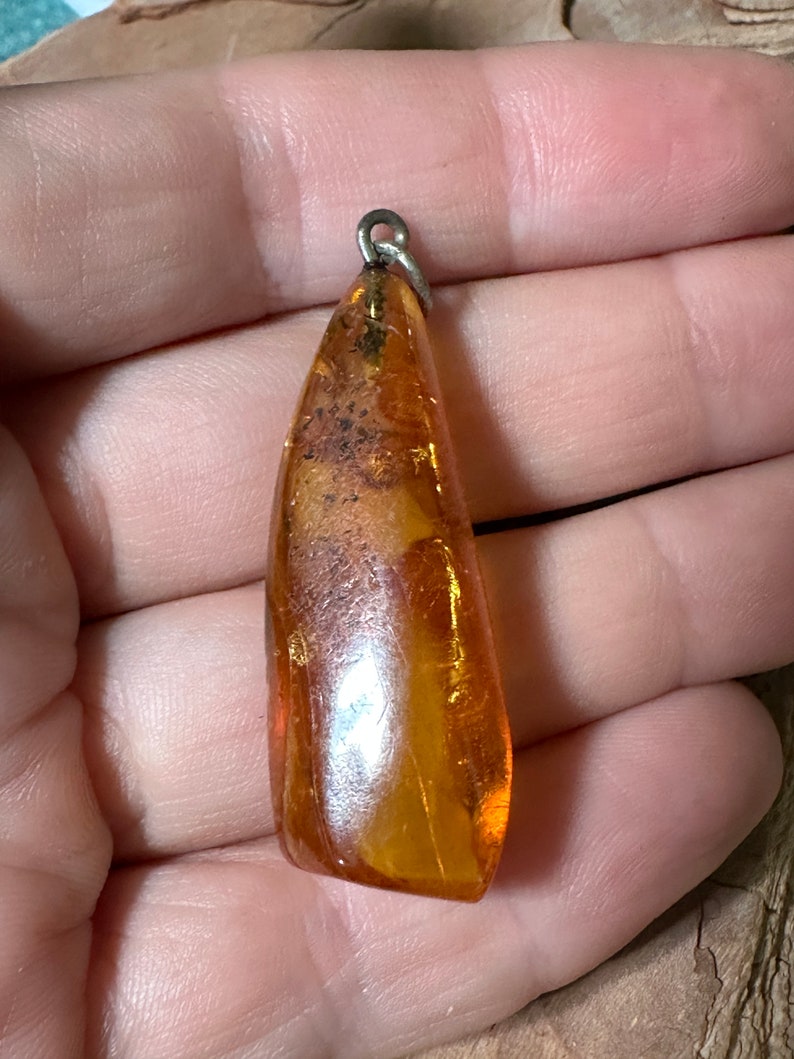 May include: A teardrop-shaped amber pendant with a silver bail. The amber is a warm, honey colour with inclusions of air bubbles and other organic matter.