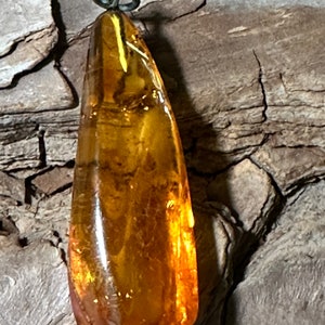 May include: A teardrop-shaped amber pendant with a silver bail. The amber is a rich, golden colour and has a smooth, polished finish.