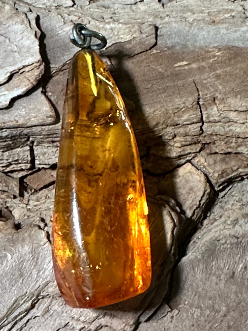May include: A teardrop-shaped amber pendant with a silver bail. The amber is a rich, golden colour and has a smooth, polished finish.