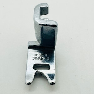 May include: Silver sewing machine foot with the text "105261 SIMANCO" printed on it.