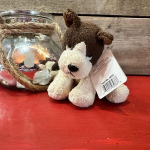 May include: Brown and white plush dog toy with a brown nose and black eyes. The toy has a white tag attached to it that says "Item No. 3033".