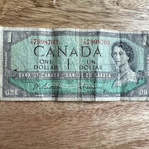 Pode incluir: Uma nota de um dólar canadense vintage com um retrato da Rainha Elizabeth II. A nota é verde e tem o texto "Canadá" e "Um dólar" impresso nela.