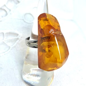 May include: A silver ring with a large, amber gemstone. The gemstone is a deep orange color and has a rough, irregular shape.
