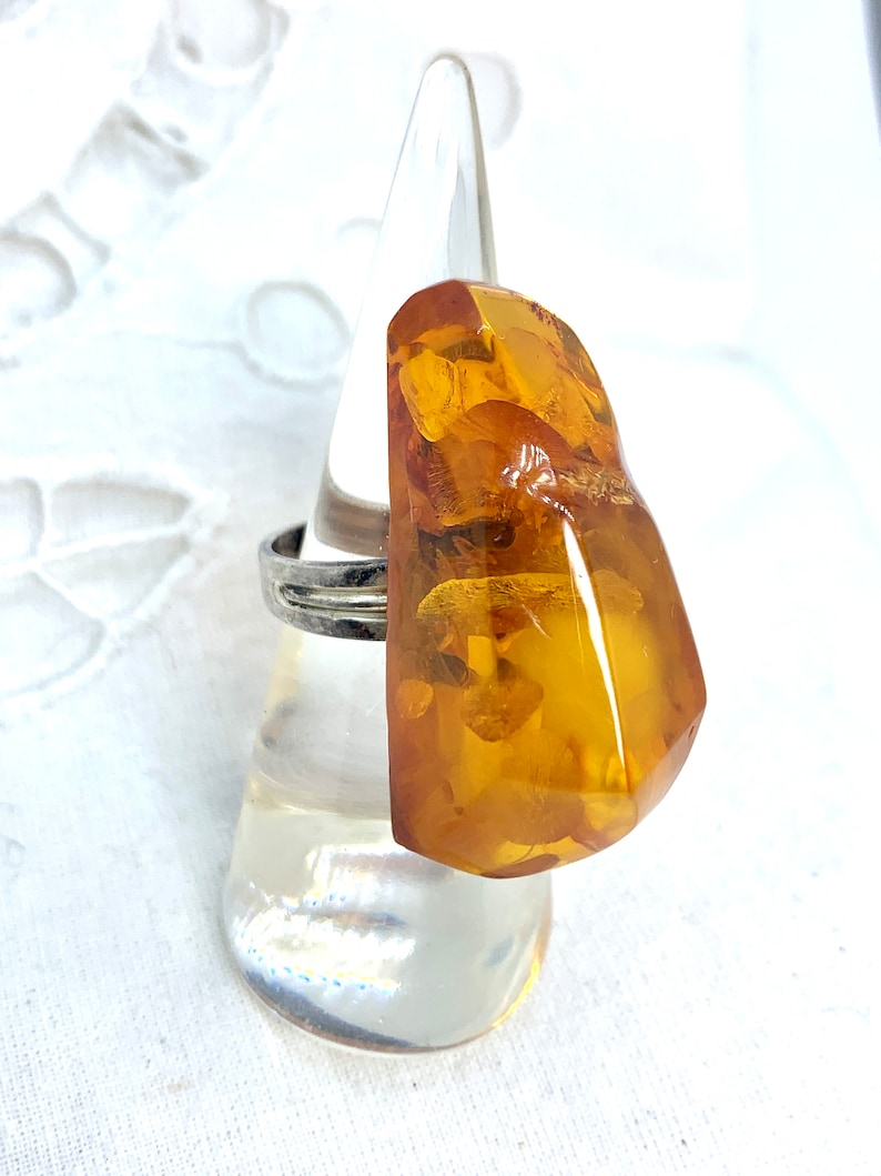 May include: A silver ring with a large, amber gemstone. The gemstone is a deep orange color and has a rough, irregular shape.