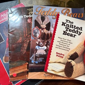 May include: Several books about teddy bears and a knitted teddy bear. The books include titles such as "Teddy Bears" and "The Knitted Teddy Bear", with patterns for clothing and accessories. The knitted bear is wearing a red waistcoat.