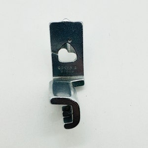 May include: A silver sewing machine foot with a heart-shaped hole and the text "SINGER 914000" on the side.