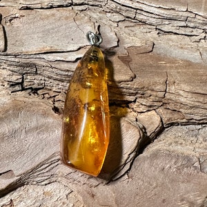 May include: A teardrop-shaped amber pendant with a silver bail. The amber is a warm honey colour with flecks of gold and brown.