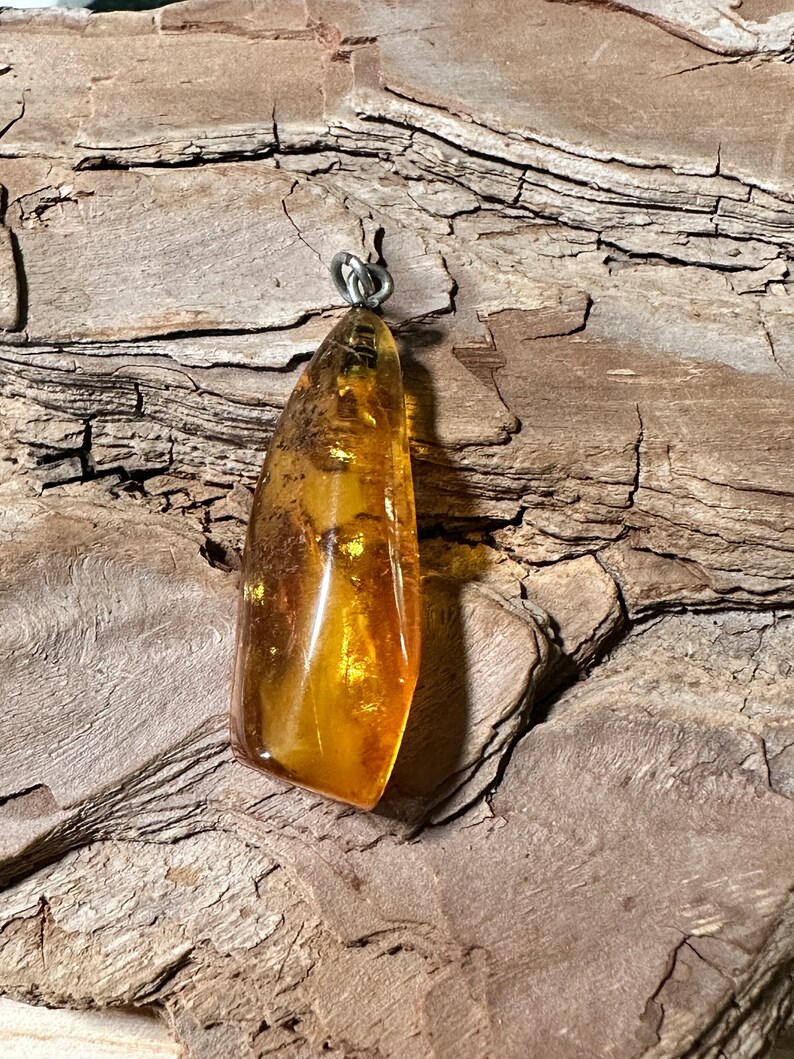 May include: A teardrop-shaped amber pendant with a silver bail. The amber is a warm honey colour with flecks of gold and brown.