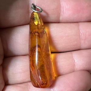 May include: A teardrop-shaped amber pendant with a silver bail. The amber is a warm, honey colour with inclusions of plant matter.
