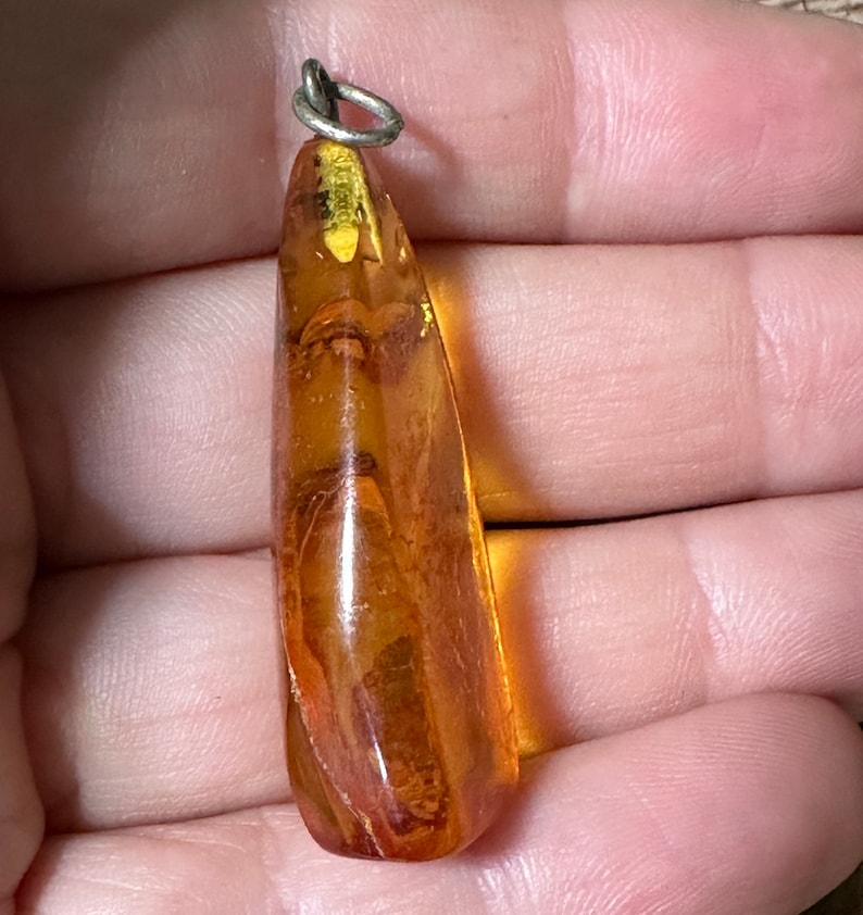 May include: A teardrop-shaped amber pendant with a silver bail. The amber is a warm, honey colour with inclusions of plant matter.