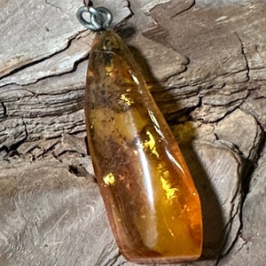 May include: A teardrop-shaped amber pendant with a silver bail. The amber is a warm honey colour with inclusions of plant matter.